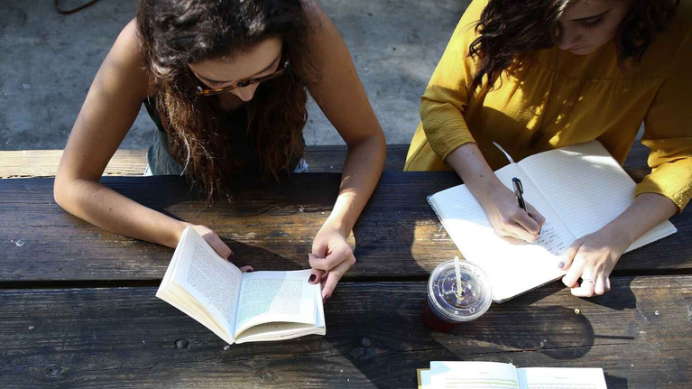 two individuals sitting at a table with books and a cup of coffee